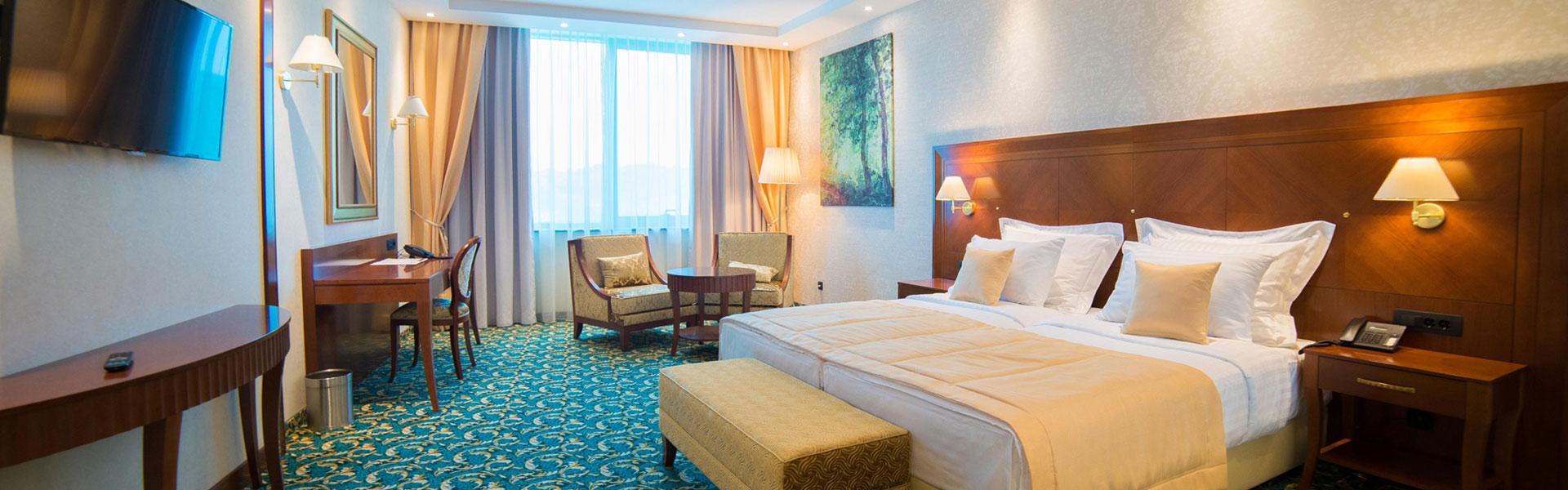 Analogna filmska fotografija hotelske spavaće sobe s velikim krevetom, drvenim uzglavljem i toplim zlatnim tonovima, smirujući i elegantan ugođaj