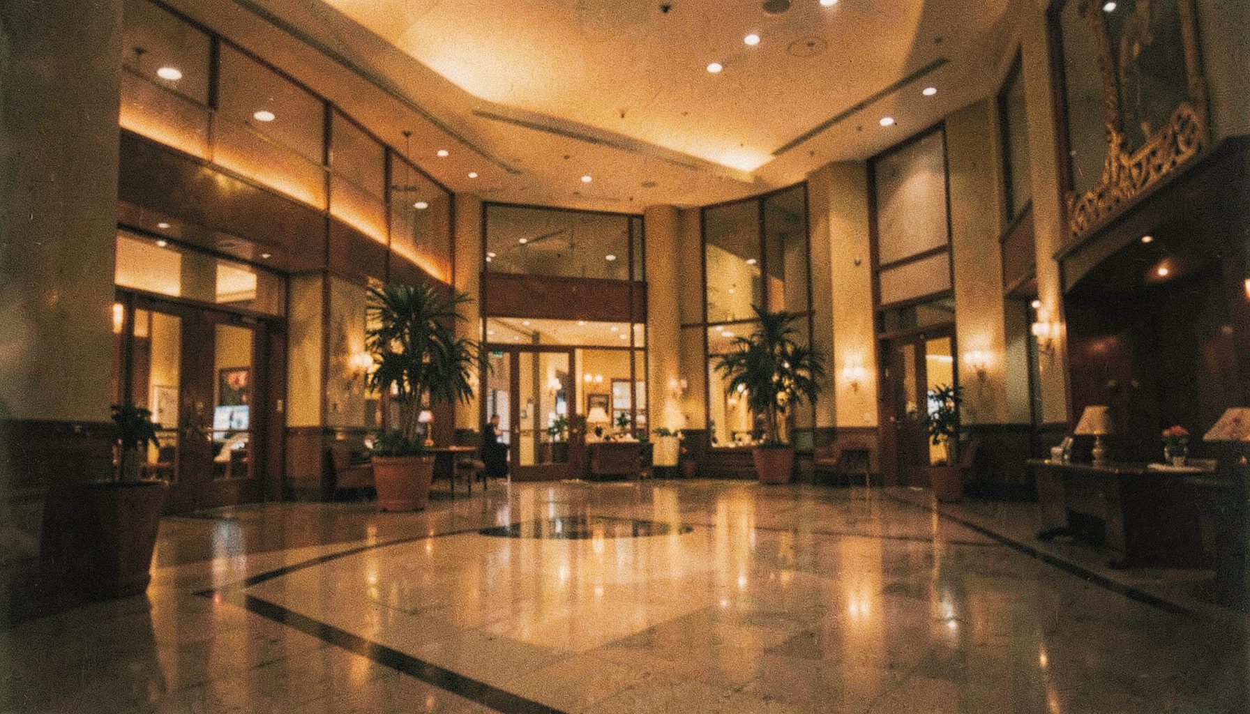 Analogna filmska fotografija hotelskog predvorja s toplim zlatnim i tamno smeđim tonovima, blještavilom lustera i mekanim sjajem na mramornim podovima